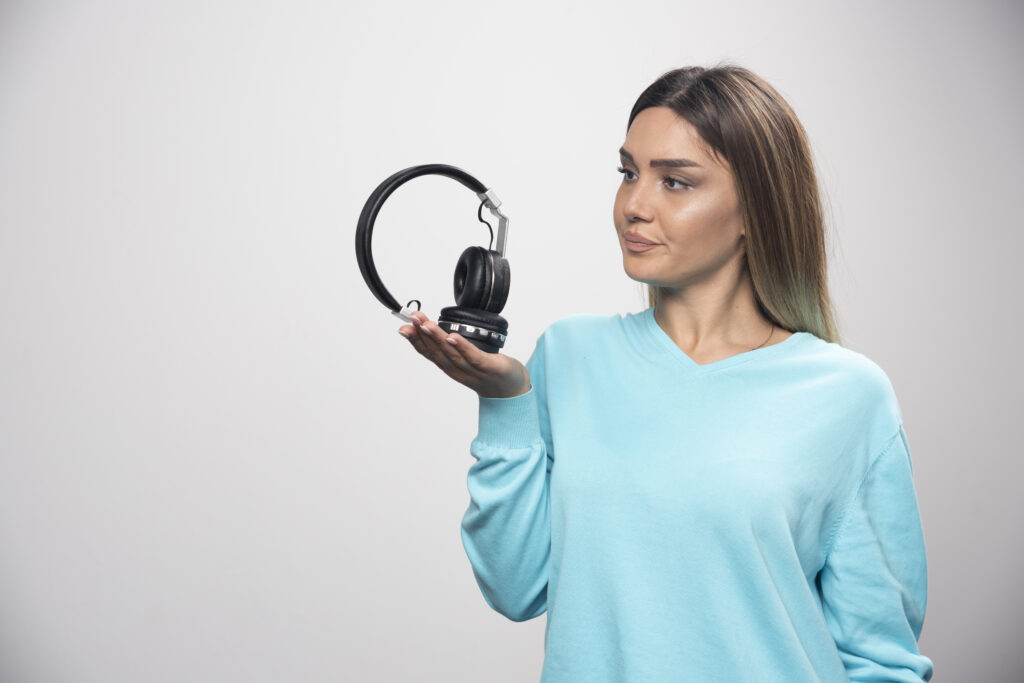 Blonde girl in blue sweatshirt holding headphones and gets ready to wear them to listen to the music